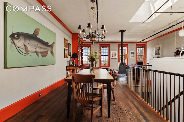 dining space featuring a skylight, a wood stove, ornamental molding, wood-type flooring, and a notable chandelier