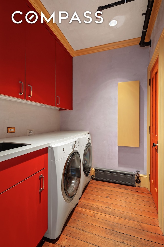 clothes washing area featuring light wood-style flooring, ornamental molding, cabinet space, and washing machine and clothes dryer