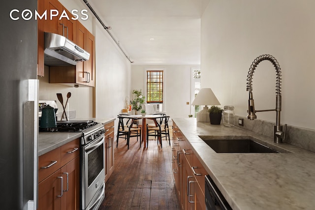 kitchen with under cabinet range hood, a sink, stainless steel gas range, brown cabinetry, and dark wood-style flooring