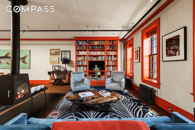 living room with wood finished floors, baseboards, a wood stove, radiator heating unit, and rail lighting