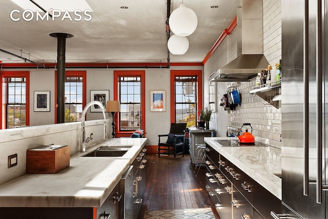 kitchen featuring a sink, wall chimney range hood, stainless steel fridge, light countertops, and dark wood-style flooring