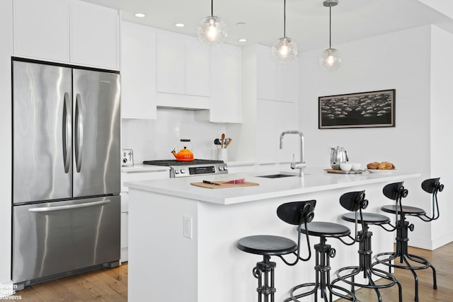 kitchen with a sink, stainless steel refrigerator, white cabinets, a kitchen breakfast bar, and range