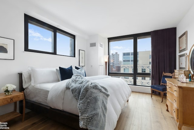 bedroom featuring visible vents, multiple windows, a city view, and light wood-style flooring