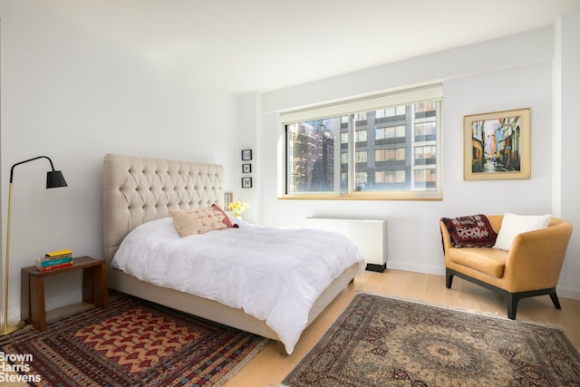 bedroom with radiator heating unit, wood finished floors, and baseboards