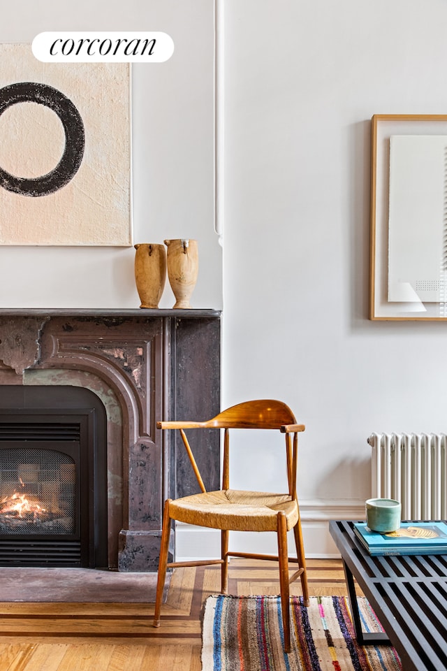 sitting room featuring a glass covered fireplace, wood finished floors, and radiator heating unit