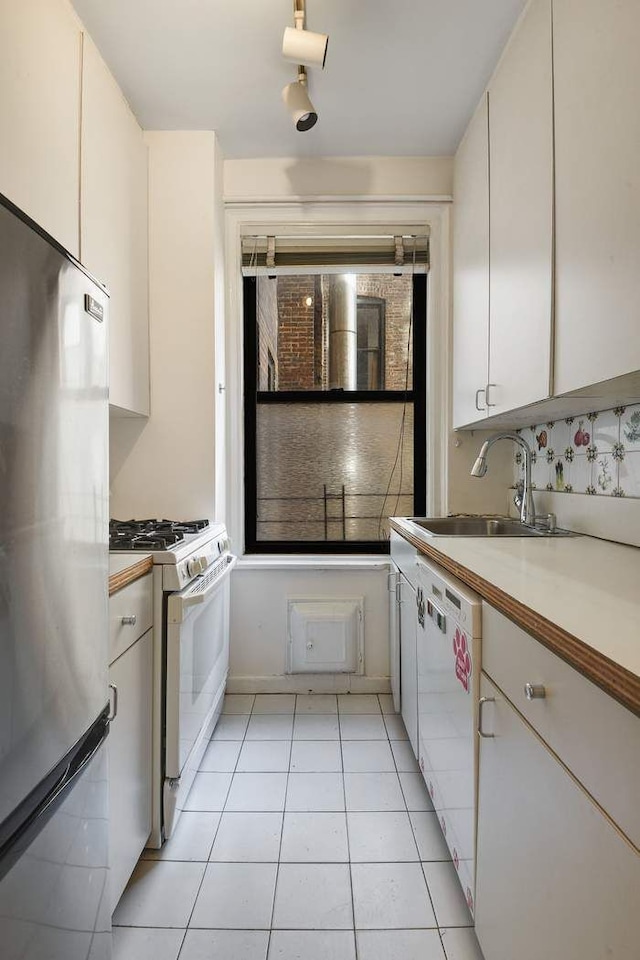 kitchen featuring a sink, white appliances, white cabinets, light countertops, and light tile patterned floors