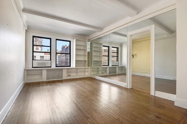 empty room featuring crown molding, beamed ceiling, baseboards, and wood-type flooring