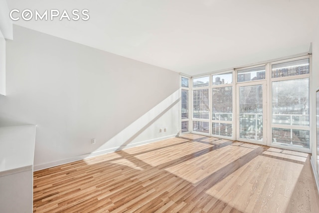 empty room with a healthy amount of sunlight, wood finished floors, and floor to ceiling windows