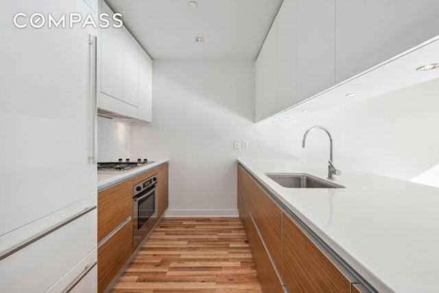 kitchen with light wood-style flooring, a sink, stainless steel appliances, white cabinets, and modern cabinets