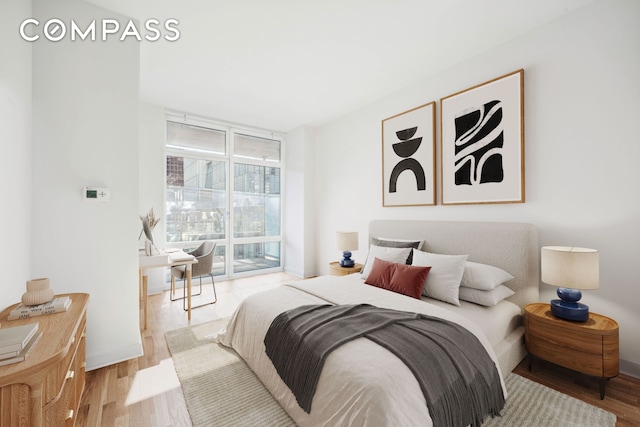 bedroom featuring floor to ceiling windows, baseboards, and wood finished floors