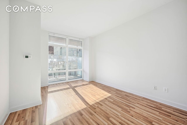 spare room with a wall of windows, baseboards, and wood finished floors