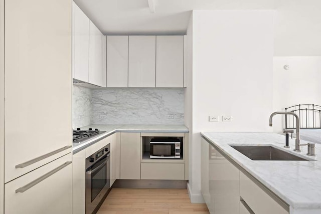 kitchen with light stone counters, light wood finished floors, a sink, stainless steel appliances, and white cabinets