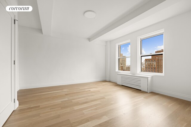 spare room with radiator, visible vents, baseboards, light wood-style floors, and beamed ceiling