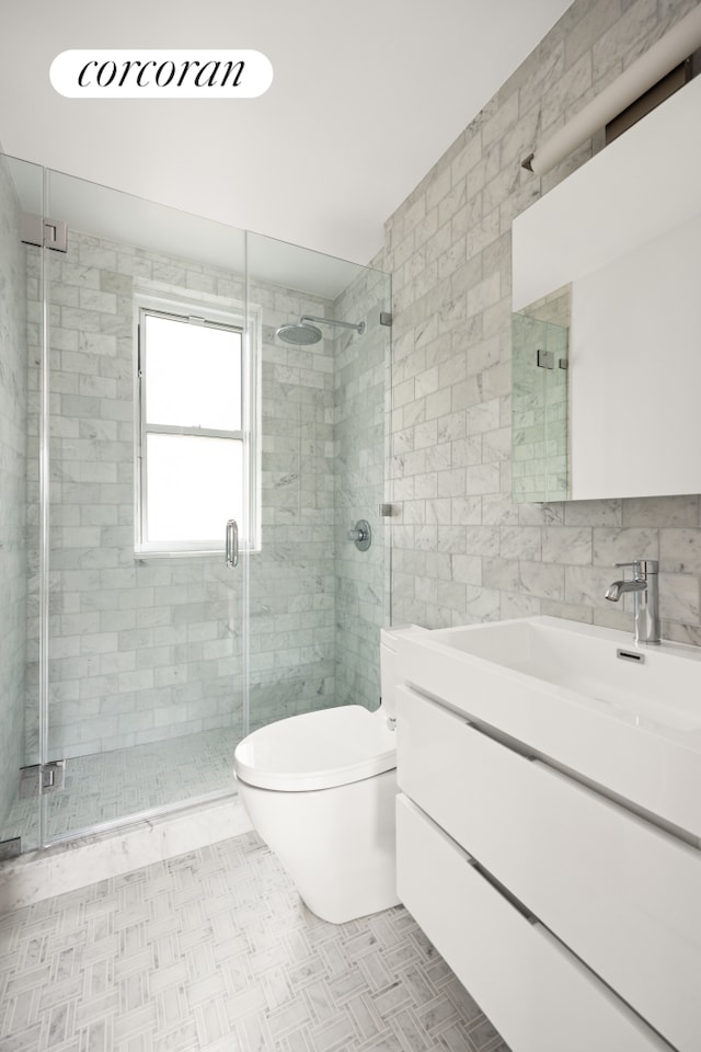 bathroom with vanity, tile walls, toilet, and a shower stall