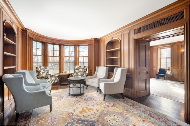 living area with built in features, wood finished floors, and ornamental molding