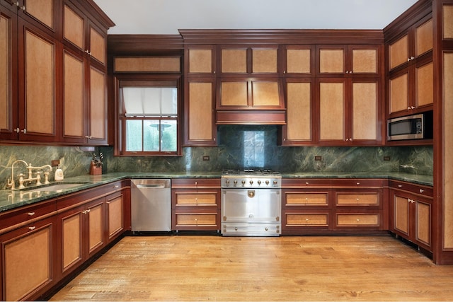 kitchen with glass insert cabinets, tasteful backsplash, a sink, light wood finished floors, and stainless steel appliances