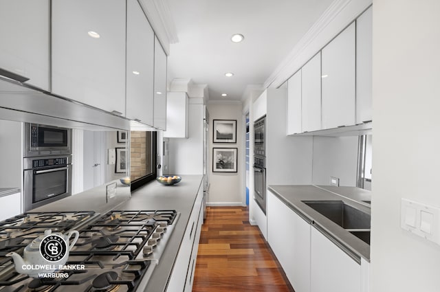 kitchen with modern cabinets, ornamental molding, dark countertops, appliances with stainless steel finishes, and white cabinets