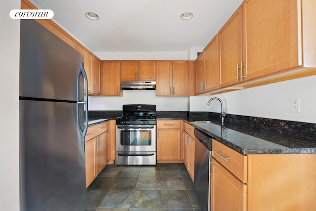 kitchen with under cabinet range hood, recessed lighting, dark stone countertops, appliances with stainless steel finishes, and a sink