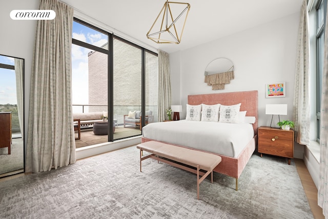 bedroom with access to exterior, a notable chandelier, wood finished floors, and expansive windows