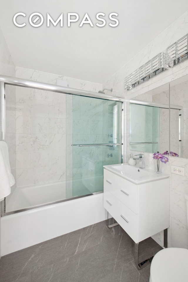 full bathroom with tile walls, toilet, enclosed tub / shower combo, marble finish floor, and vanity