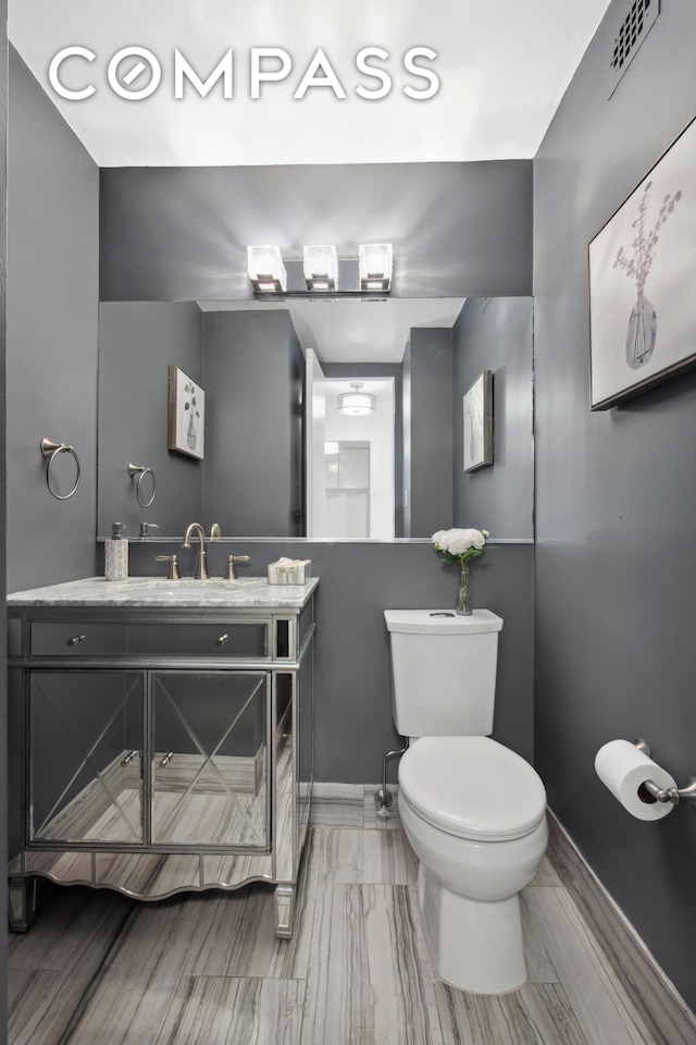 half bath featuring vanity, toilet, baseboards, and visible vents