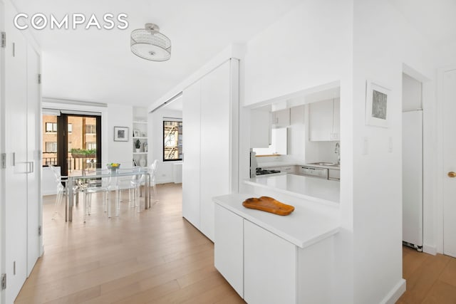 kitchen with refrigerator, a sink, light countertops, white cabinets, and light wood-style floors