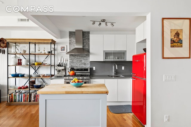 kitchen with stainless steel gas range oven, wall chimney range hood, refrigerator, wood counters, and a sink