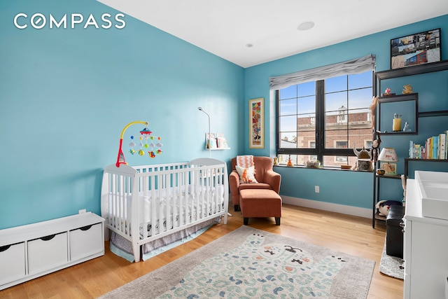 bedroom with a crib, wood finished floors, and baseboards