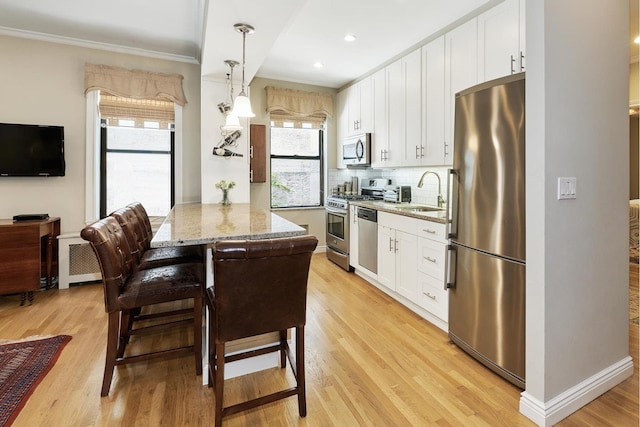 kitchen with light wood-type flooring, decorative backsplash, appliances with stainless steel finishes, white cabinets, and a sink