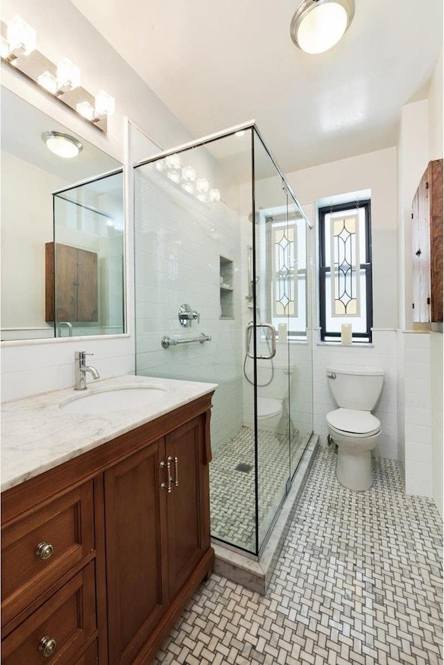 full bathroom with vanity, tile walls, toilet, and a shower stall