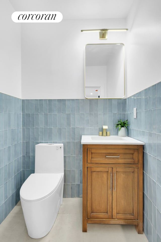 half bath with toilet, tile walls, wainscoting, and vanity