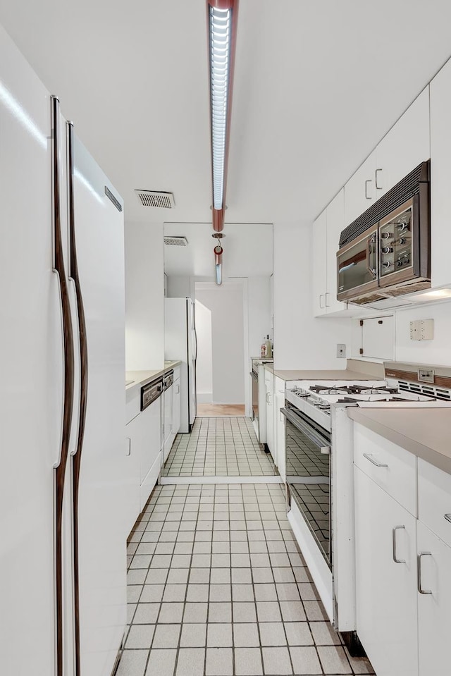 kitchen with visible vents, light countertops, light tile patterned flooring, white cabinets, and white appliances