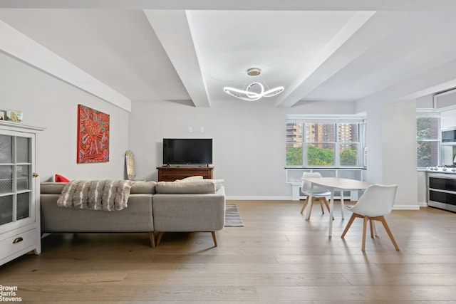 living area featuring an inviting chandelier, beamed ceiling, wood finished floors, and a healthy amount of sunlight