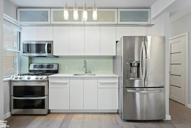 kitchen with a sink, light countertops, white cabinets, light wood-style floors, and appliances with stainless steel finishes