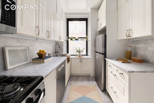 kitchen featuring a sink, stainless steel appliances, light stone counters, and white cabinets