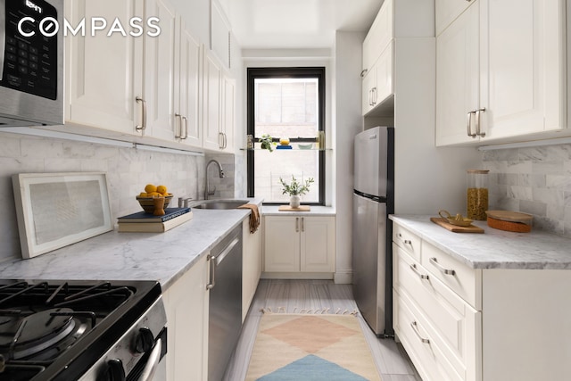 kitchen with light stone countertops, appliances with stainless steel finishes, a sink, white cabinetry, and tasteful backsplash