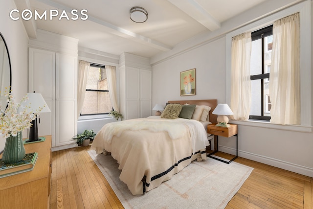 bedroom featuring light wood finished floors, beamed ceiling, and baseboards