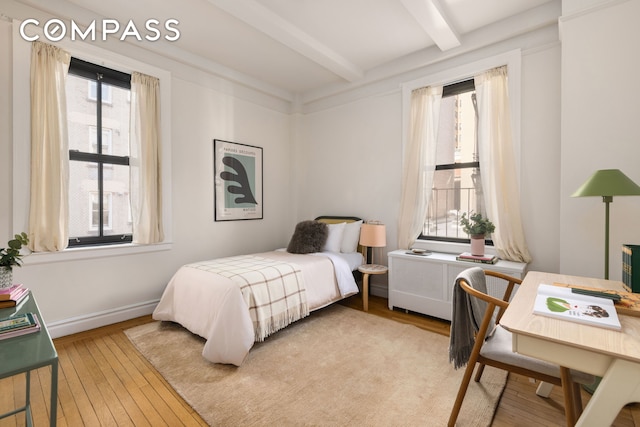 bedroom featuring beamed ceiling, multiple windows, radiator, and wood-type flooring