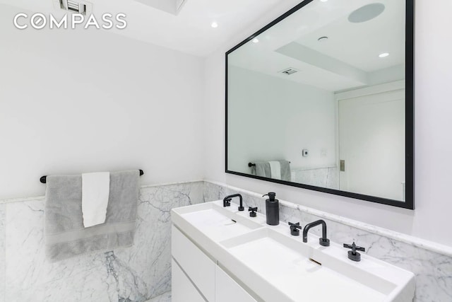 bathroom featuring a sink, tile walls, recessed lighting, double vanity, and wainscoting