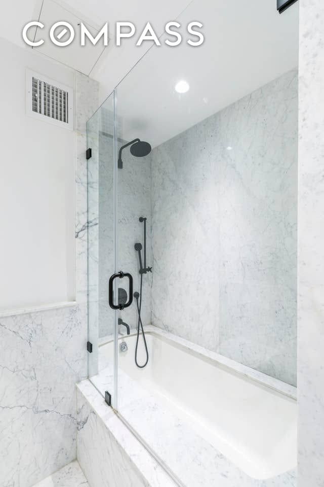 full bathroom with tile walls, a tub with marble appearance, visible vents, and a marble finish shower