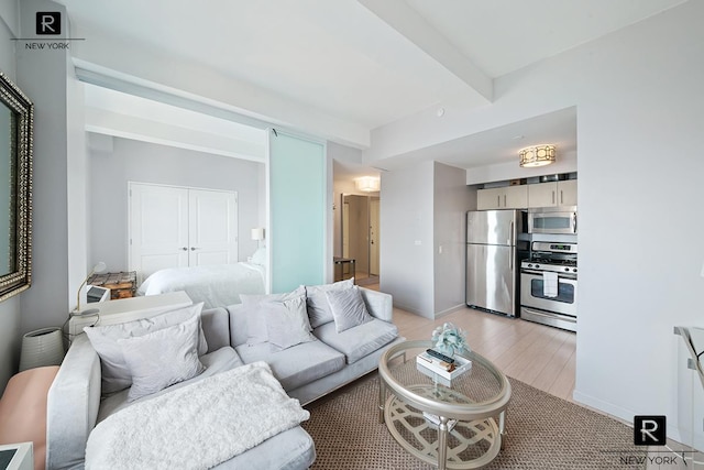 living room featuring beamed ceiling, baseboards, and light wood finished floors