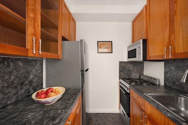 kitchen with white microwave, decorative backsplash, brown cabinetry, gas stove, and a sink