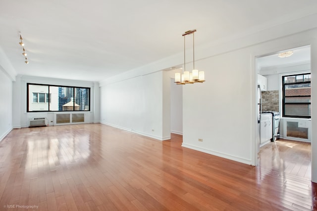 unfurnished room featuring baseboards, light wood-type flooring, an inviting chandelier, and ornamental molding