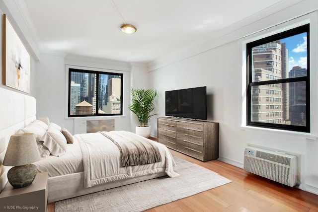 bedroom with baseboards, wood finished floors, ornamental molding, and a wall mounted AC