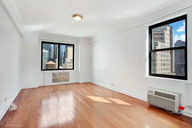 spare room featuring a view of city, an AC wall unit, ornamental molding, wood finished floors, and baseboards