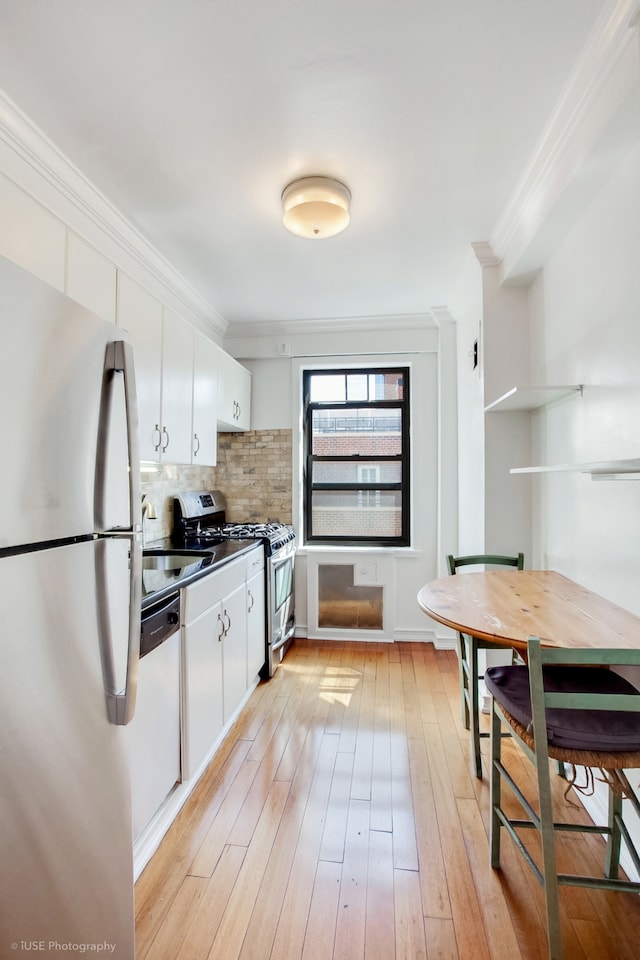 kitchen with tasteful backsplash, ornamental molding, light wood-style floors, white cabinets, and stainless steel appliances