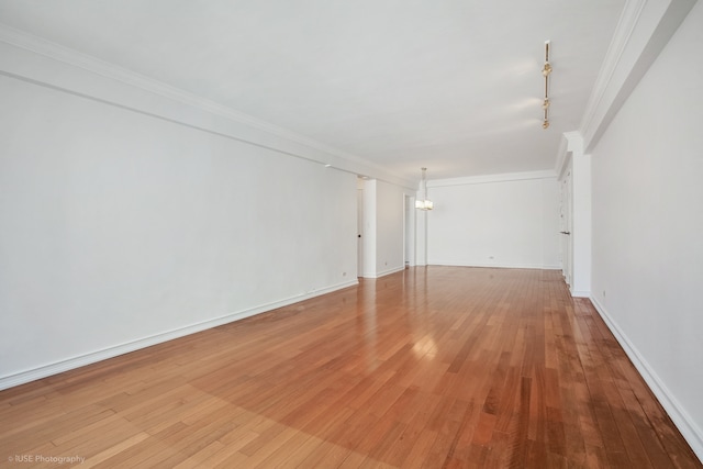 empty room with light wood-type flooring, baseboards, a notable chandelier, and ornamental molding