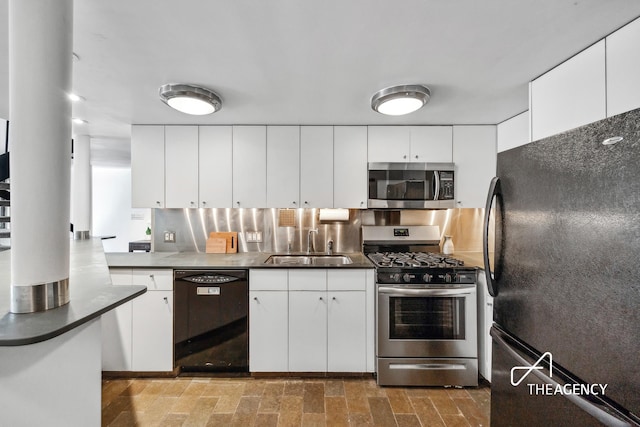 kitchen featuring dark countertops, white cabinets, black appliances, and a sink