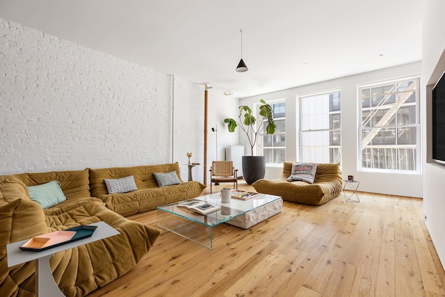 living area featuring wood-type flooring, brick wall, and radiator heating unit