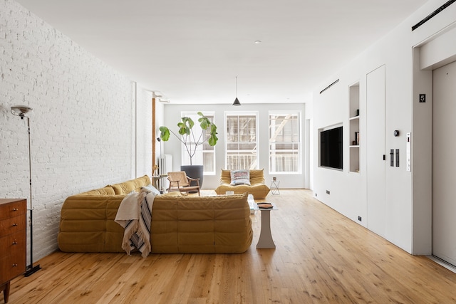 living area with light wood-style flooring, elevator, and brick wall